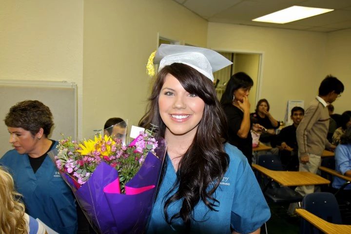 A smiling graduate holding flowers